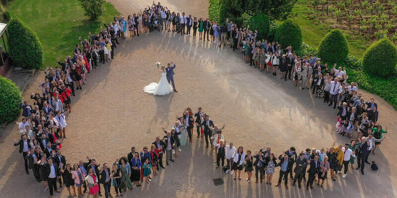 Vue aérienne d'un grand rassemblement de personnes qui se tiennent en formation de cœur, créant une image mémorable pour un mariage. Les mariés se tiennent au centre de la formation.